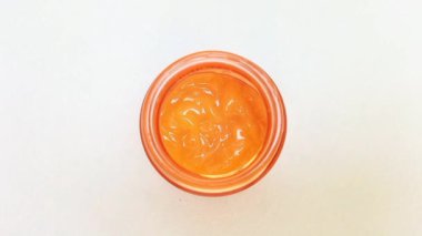 Cam bir kaptaki C vitamini kremi yakınlaştırırken beyaz arkaplanda dönüyor. sarı-turuncu C vitamini kremi gibi hafif jel.