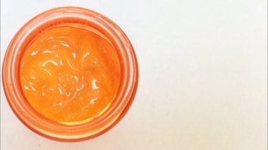 Cam bir kaptaki C vitamini kremi. Beyaz zemin üzerinde fotokopi alanı ile birlikte dönüyor. Sarı-turuncu C vitamini kremi gibi hafif jel. Kapat, üst görünüm