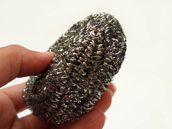Рука, держащая в руках скраб из нержавеющей стали, металлическую губку на белом фоне, стальную шерстяную прокладку для мытья посуды, скраб-бутон