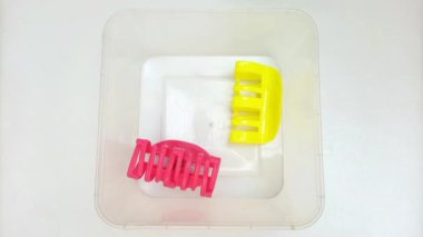 Beyaz arka planda şeffaf bir kutuyu dolduran renkli plastik saç tokalarının hareketini durdur. Kadın saç aksesuarları. Moda bir aksesuar. Modaya uygun aksesuarlar.