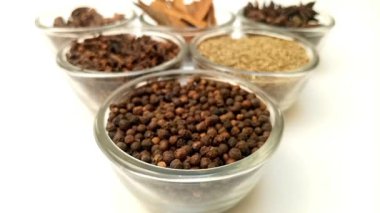 Arka planda cam kaselerde çeşitli aromatik baharatlar ve bitkiler bulunan bir kase karabibere odaklan..