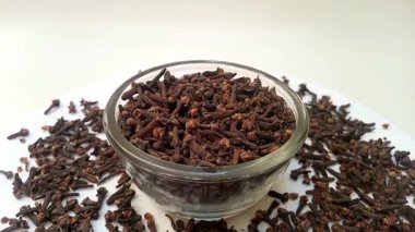 Etrafına saçılmış cam bir kapta karanfiller, beyaz arka plan, merkez çerçeve, yakınlaştırma, kapama, otlar ve baharatlar.