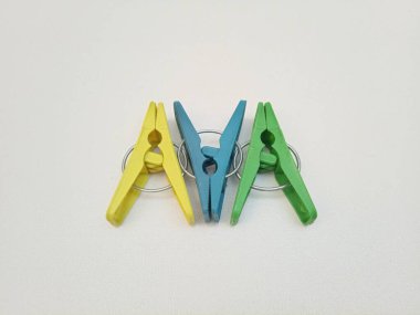 Giysi iğneleri, üç tane çok renkli plastik çamaşır tokası ya da beyaz arka planda elbise askısı.