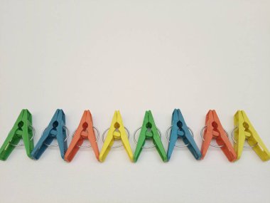 Giysi iğneleri, çok renkli plastik çamaşır mandalları ya da elbise askıları beyaz arka planda en altta bir çizgide.