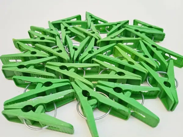 Beyaz arka planda bir sürü yeşil çamaşır klipsi, ev için plastik mandallar ya da elbise askıları.