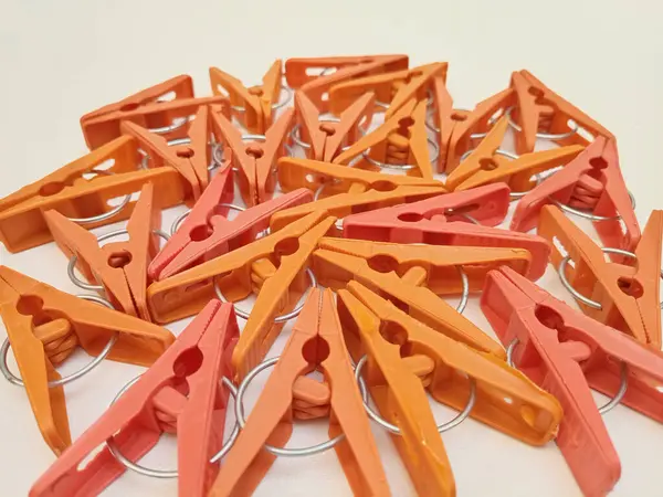 Beyaz arka planda birçok turuncu çamaşır klipsleri, ev için plastik mandallar ya da elbise askıları.