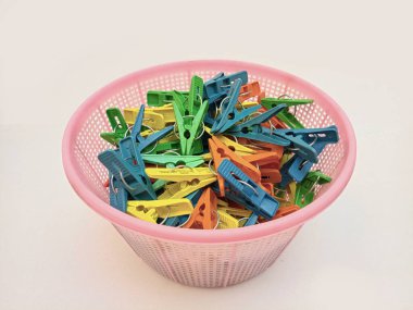 Beyaz arka planda çamaşır tokası dolu bir sepet, çok renkli çamaşır mandalları ya da ev için elbise askıları.