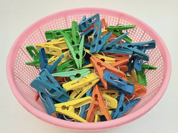 Beyaz arka planda çamaşır tokası dolu bir sepet, çok renkli plastik çamaşır mandalları ya da ev için elbise askıları, kapat.