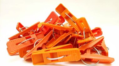 Beyaz arka planda dönen turuncu çamaşır mandalları, ev için plastik mandallar ya da elbise askıları.