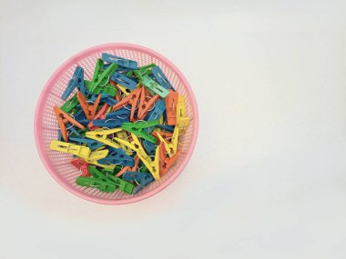 Beyaz arka planda izole edilmiş çamaşır iğneleriyle dolu bir sepet, çok renkli plastik çamaşır mandalları veya elbise askıları.
