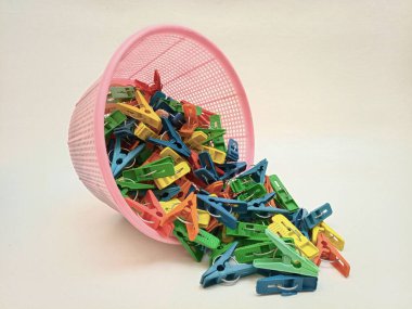 Beyaz arka planda sepetten düşen mandallar, çok renkli plastik çamaşır mandalları ya da elbise askıları.