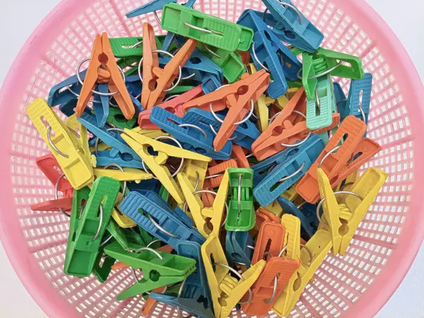 Beyaz arka planda çamaşır tokası dolu bir sepet, çok renkli plastik çamaşır mandalları ya da mandallar, yakın çekim, üst görüş.