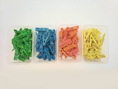 Beyaz arkaplandaki konteynırlarda farklı renkte çamaşır klipsleri, çok renkli plastik mandallar veya elbise askıları, üst görünüm