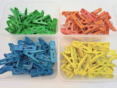 Beyaz arka plandaki konteynırlarda farklı renkte çamaşır klipsleri, ev için çok renkli plastik iğne setleri veya elbise askıları, kapat