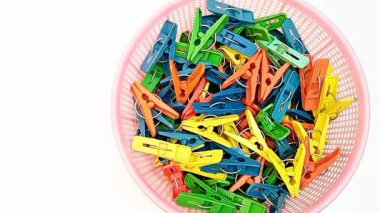 Beyaz arka planda hareket eden bir sepet dolusu çamaşır iğnesi, çok renkli çamaşır tokaları ya da ev için elbise askıları.