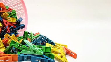 Beyaz arka planda hareket eden sepetten düşen broşlar, çok renkli plastik çamaşır tokaları veya elbise askıları,