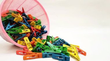 Beyaz arka planda sepetten düşen broşlar, çok renkli plastik çamaşır tokaları ya da elbise askıları.