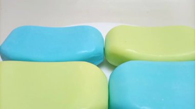 Sabun barı. Beyaz arka planda hareket eden banyo için mavi ve sarı sabunlar. Vücut ve yüz için aromatik sabun. Mavi ve sarı banyo sabunu parçaları. Kapat..
