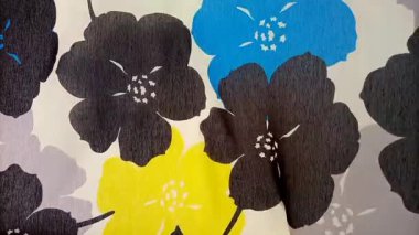 Çiçek desenli kumaş detayı rüzgar, doku, kalın, estetik, sadeleştirilmiş çiçek deseni siyah, mavi ve sarı çiçeklerle gri ve beyaz arka planda sallanıyor.