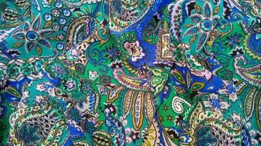 Paisley desenli kumaş detayı, kıvrımlı zumlama arkaplanı, kıvrımlı, gözyaşı damlası şekilli motifleri, mavi ve yeşil gibi canlı renkler, desen