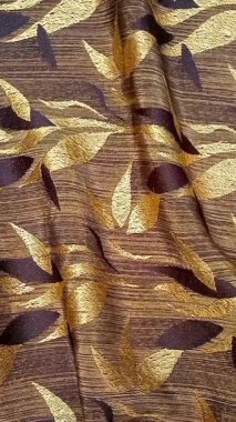 Tekstil kumaş hareketli arka planda kahverengi ve altının çeşitli tonlarında tekrarlanan yapraklar var. Çiçek veya yaprak benzeri motifler simetrik desenlerde sıralanmış, basitleştirilmiş.