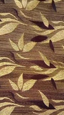 Tekstil kumaş hareketli arka planda kahverengi ve altının çeşitli tonlarında tekrarlanan yapraklar var. Çiçek veya yaprak benzeri motifler simetrik desenlerde sıralanmış, basitleştirilmiş.