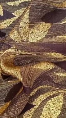 Tekstil kumaş hareketli arka planda kahverengi ve altının çeşitli tonlarında tekrarlanan yapraklar var. Çiçek veya yaprak benzeri motifler simetrik desenlerde sıralanmış, basitleştirilmiş.