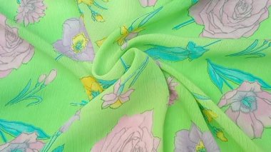 Çiçek desenli kıvrımlı güller, nergisler ve pembe, mor ve sarı tonlarında diğer çiçekler gibi çeşitli çiçekler parlak yeşil bir arkaplana saçılmıştır.