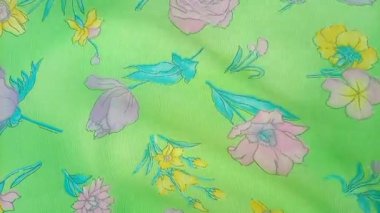 Dalgalanan çiçek deseninde güller, nergisler ve pembe, mor ve sarı tonlarında diğer çiçekler parlak yeşil bir arkaplanda serpilmiştir.