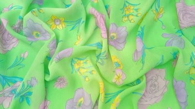 Buruşuk çiçek deseninde güller, nergisler ve pembe, mor ve sarı tonlarında diğer çiçekler parlak yeşil bir arka planda serpilmiştir.