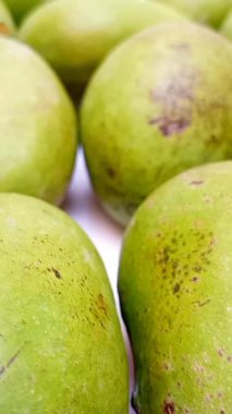 Beyaz arka planda taze yeşil mango meyveleri dönüyor, tropikal meyveler, olgunlaşmamış mangolar turşu için, dikey şarjör.