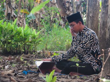 Asyalı Müslüman bir adam oturuyor ve Kuran okuyor. Ormanın ortasındaki barış onu dindar ve geleneksel bir atmosfer haline getiriyor.