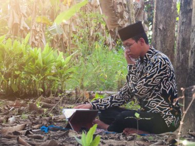 Asyalı Müslüman bir adam oturuyor ve Kuran okuyor. Ormanın ortasındaki barış onu dindar ve geleneksel bir atmosfer haline getiriyor.