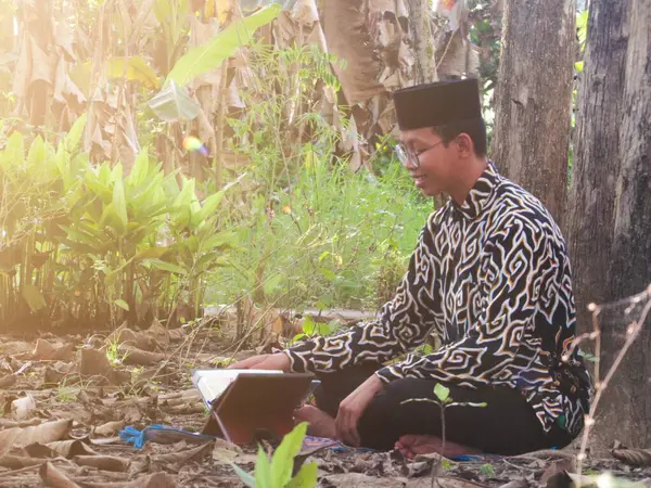 Asyalı Müslüman bir adam oturuyor ve Kuran okuyor. Ormanın ortasındaki barış onu dindar ve geleneksel bir atmosfer haline getiriyor.