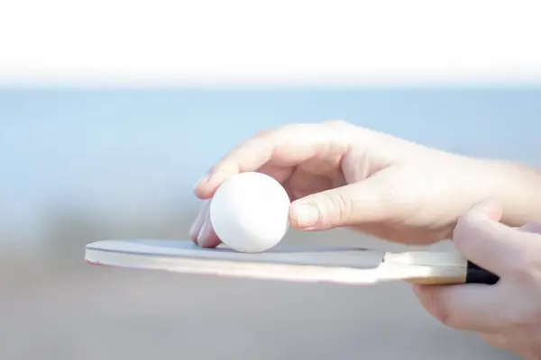 Mavi arka planda, deniz ve beyaz gündüz kuşağının olduğu bir masa tenisi topu ve kürek el ele tutuştu. Kompozisyon, sporu, aktif bir yaşam tarzını ve oyunun enerjisini taşır.