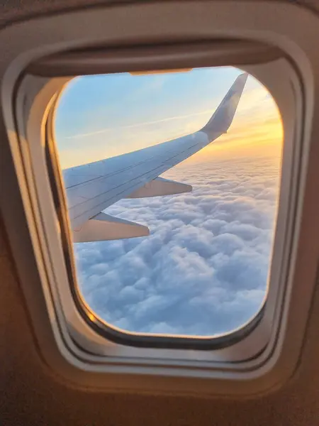 Bir uçak penceresinden bakın: pencere çerçevesi, uçak kanadı, yükselen ya da batan güneş ve bulutlar. Atmosferik seyahat ve ilham verici fotoğraf