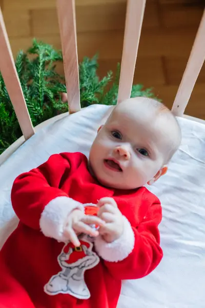Parlak kırmızı Noel kıyafetli küçük bir bebek yuvarlak bir ahşap beşikte yatıyor. Memlekette şenlik havası.