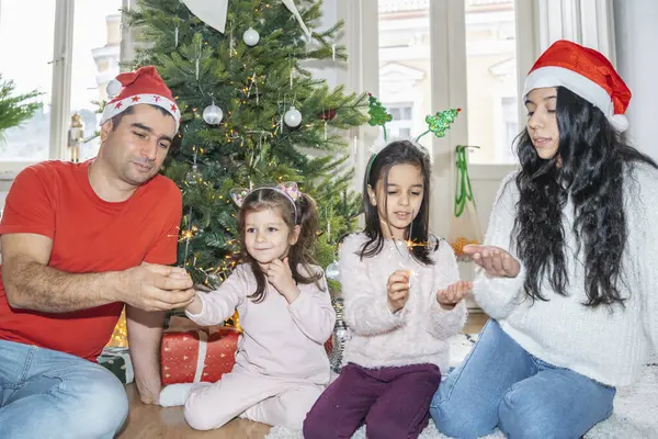 Çocuklar neşeli bir Noel ağacının yanında maytap yakıyor. Noel ve yeni yıl için mutlu anlar, aile sıcaklığı, ve büyülü tatil atmosferi.