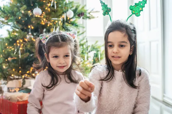 Çocuklar neşeli bir Noel ağacının yanında maytap yakıyor. Noel ve yeni yıl için mutlu anlar, aile sıcaklığı, ve büyülü tatil atmosferi.