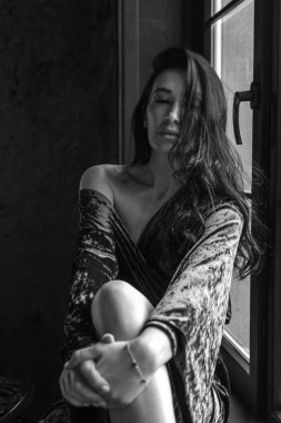 Zarif ve baştan çıkarıcı kıyafetli şehvetli bir esmer, banyo ve mutfağın bulunduğu modern bir çatı katında poz veriyor. Lüks, konfor ve estetik bir atmosfer..