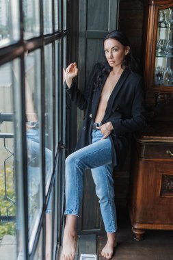 Zarif ve baştan çıkarıcı kıyafetli şehvetli bir esmer, banyo ve mutfağın bulunduğu modern bir çatı katında poz veriyor. Lüks, konfor ve estetik bir atmosfer..