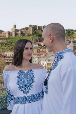 Damat geline evlilik teklifi ederken, bir nişan yüzüğü takıp nazikçe yanağından öpüyor. Çift geleneksel Ukrayna nakışlı düğün kıyafetleri giyer, Tbi 'nin manzaralı arka planına karşı sevgi ve bağlılığı kutlar.