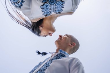 Geleneksel Ukrayna nakışlı düğün kıyafeti giymiş yeni evliler, Gürcistan 'ın Tiflis kentindeki modern cam mimarinin önünde zarif bir şekilde poz veriyorlar. Beyaz gelinlikli gelin bir buket narin mavi çiçek tutuyor. Kültürünün mükemmel bir karışımı.