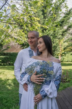 Geleneksel Ukrayna nakışlı düğün kıyafeti giymiş yeni evliler, Gürcistan 'ın Tiflis kentindeki modern cam mimarinin önünde zarif bir şekilde poz veriyorlar. Beyaz gelinlikli gelin bir buket narin mavi çiçek tutuyor. Kültürünün mükemmel bir karışımı.