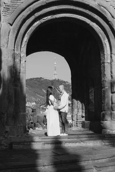 Geleneksel Ukrayna işlemeli düğün kıyafeti giyen yeni evli bir çift, Gürcistan 'ın Tiflis kentindeki antik bir kemerin altında romantik bir öpücük paylaşıyor. Gelin beyaz bir gelinlik giyiyor ve damat onu sevgiyle kucaklıyor. Bir yaz tatili düğünü.