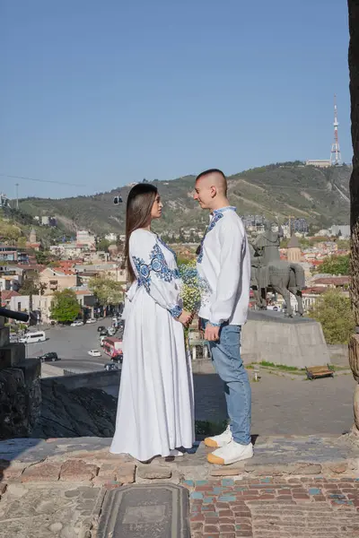 Geleneksel Ukrayna işlemeli düğün kıyafeti giyen yeni evli bir çift, Gürcistan 'ın Tiflis kentindeki antik bir kemerin altında romantik bir öpücük paylaşıyor. Gelin beyaz bir gelinlik giyiyor ve damat onu sevgiyle kucaklıyor. Bir yaz tatili düğünü.
