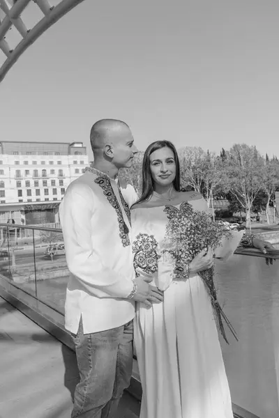 Geleneksel Ukrayna nakışlı düğün kıyafeti giymiş yeni evliler, Gürcistan 'ın Tiflis kentindeki modern cam mimarinin önünde zarif bir şekilde poz veriyorlar. Beyaz gelinlikli gelin bir buket narin mavi çiçek tutuyor. Kültürünün mükemmel bir karışımı.