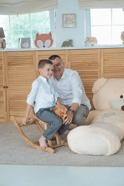 Samimi bir aile fotoğrafı, hassas bir beklenti anını yakalıyor. Siyah bluz ve düğmesiz beyaz gömlek giyen hamile anne elini nazikçe karnına koyar. Beyaz gömlekli baba, onun arkasında korunuyor.