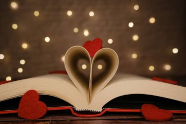 Kırmızı keçeli kalpler ve bokeh ışıklarıyla süslenmiş, kalp şeklinde sayfalar oluşturan açık bir kitap.