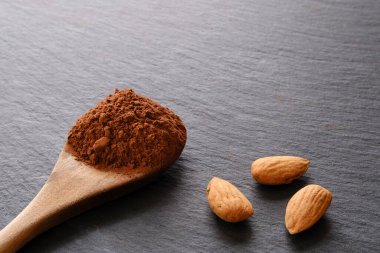 Arkaplanda bir kaşık kakao tozu ve badem.